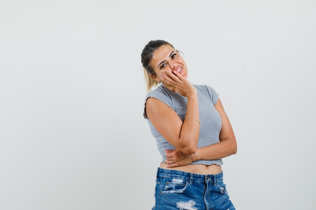 Jeune femme tenant la main sur la joue en t-shirt, short et à la joie