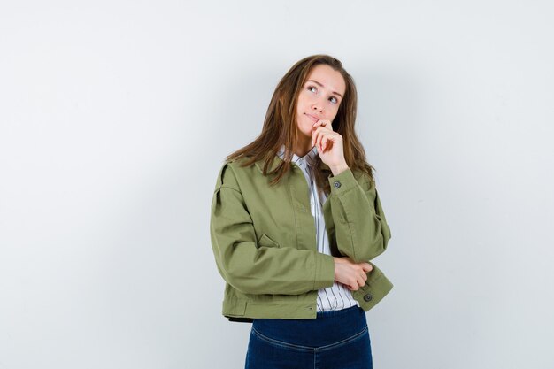 Jeune femme tenant la main sur le menton en chemise et regardant pensive, vue de face.