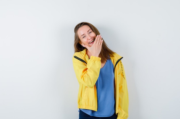 Jeune femme tenant la main sur le menton en t-shirt, veste et très jolie. vue de face.