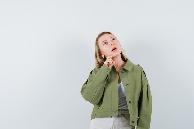 Jeune femme tenant la main sur le menton en veste, pantalon et à la pensif. vue de face.