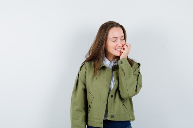 Jeune femme tenant la main près de la bouche en chemise, veste et l'air paisible. vue de face.