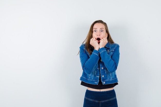 Jeune femme tenant la main près de la bouche ouverte en blouse, veste et l'air choquée, vue de face.