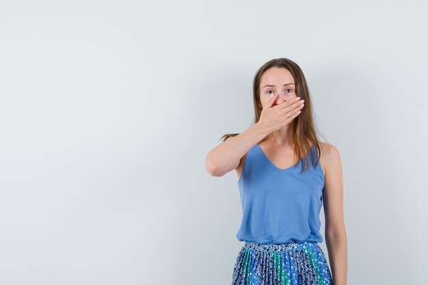 Jeune femme tenant la main sur sa bouche en chemisier bleu, jupe et à la dégoûté, vue de face.