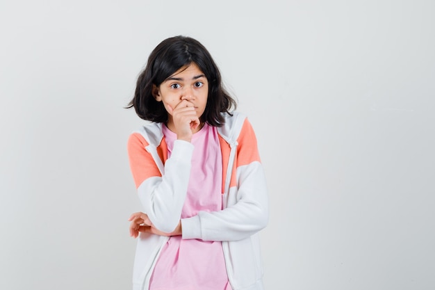 Jeune femme tenant la main sur sa bouche tout en regardant ailleurs en veste, chemise rose et à la recherche attentive.