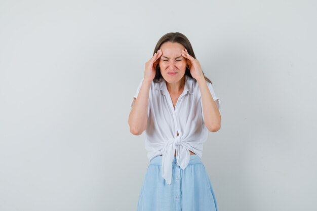 Jeune femme tenant la main sur sa tempe en chemisier, jupe et à la fatigue