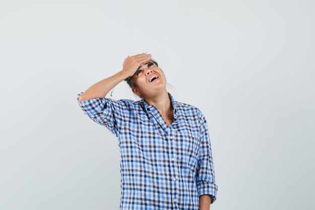 Jeune femme tenant la main sur son front en chemise à carreaux.