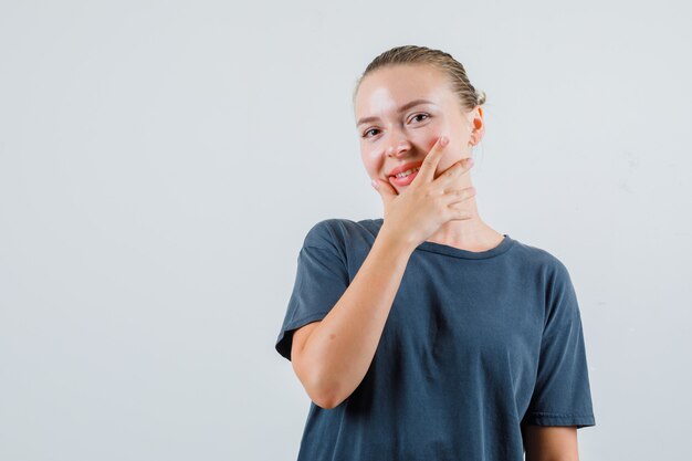 Jeune femme tenant la main sur son menton en t-shirt gris et à la joyeuse