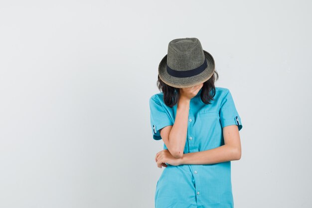 Jeune femme tenant la main sur son visage en chemise bleue, chapeau et à la colère.