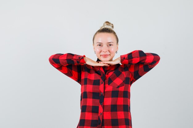 Jeune femme tenant la main sous le menton en chemise à carreaux et à la jolie vue de face.