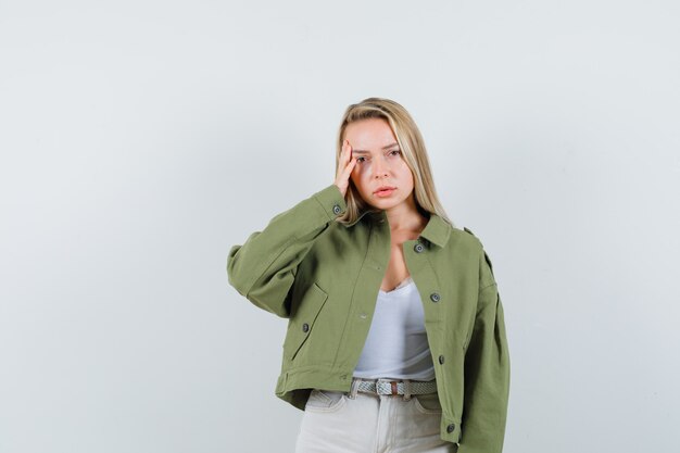 Jeune femme tenant la main sur les tempes en veste, pantalon et à la colère, vue de face.