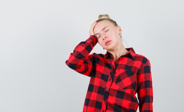 Photo gratuite jeune femme tenant la main sur la tête en chemise à carreaux et à la fatigue, vue de face.