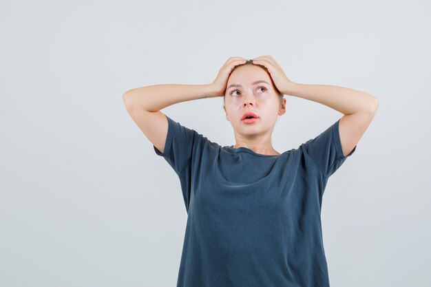 Jeune femme tenant la main à la tête en t-shirt gris et à la réflexion