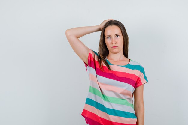 Jeune femme tenant la main sur la tête en t-shirt et à la sombre. vue de face.