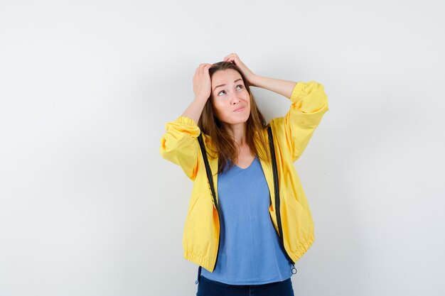 Jeune femme tenant la main sur la tête en t-shirt, veste et hésitante. vue de face.