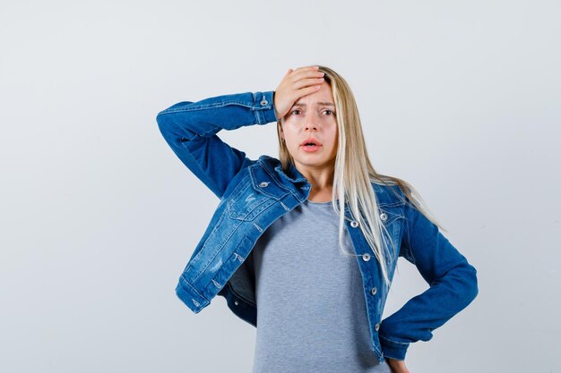 Jeune femme tenant la main sur la tête en t-shirt, veste en jean, jupe et à l'oubli.