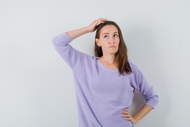 Jeune femme tenant la main sur la tête tout en regardant ailleurs en chemisier lilas et à la pensif