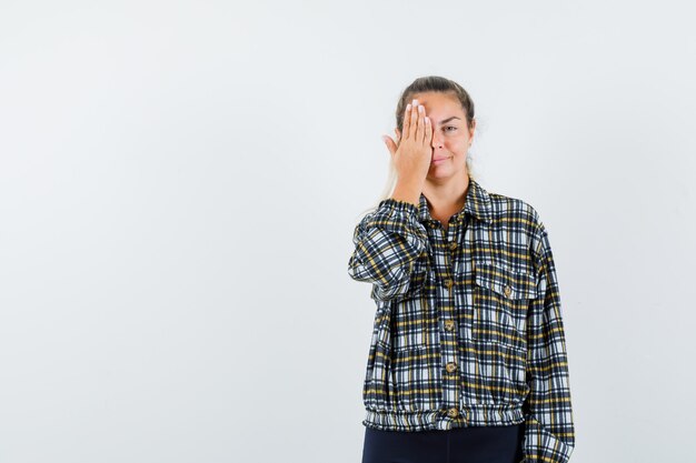 Jeune femme tenant la main sur les yeux en chemise, short et à la ravissante vue de face.