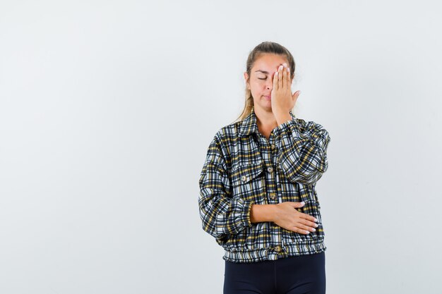 Jeune femme tenant la main sur les yeux en chemise, short et à la recherche de calme. vue de face.