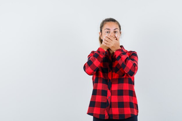 Jeune femme tenant les mains sur la bouche en chemise à carreaux et à la choqué