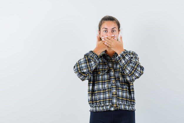 Photo gratuite jeune femme tenant les mains sur la bouche en chemise, short et à la peur, vue de face.