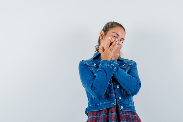 Jeune femme tenant les mains sur la bouche en chemise, veste et à la joyeuse. vue de face.