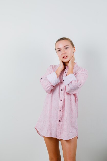 Jeune femme tenant les mains sur le cou en chemise rose et à la séduisante