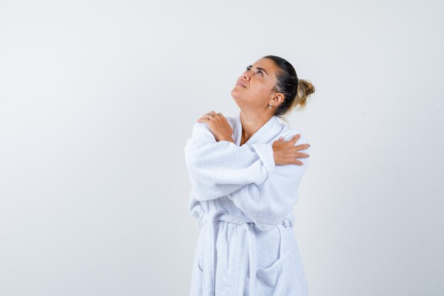 Jeune femme tenant les mains croisées sur l'épaule en peignoir et l'air positif