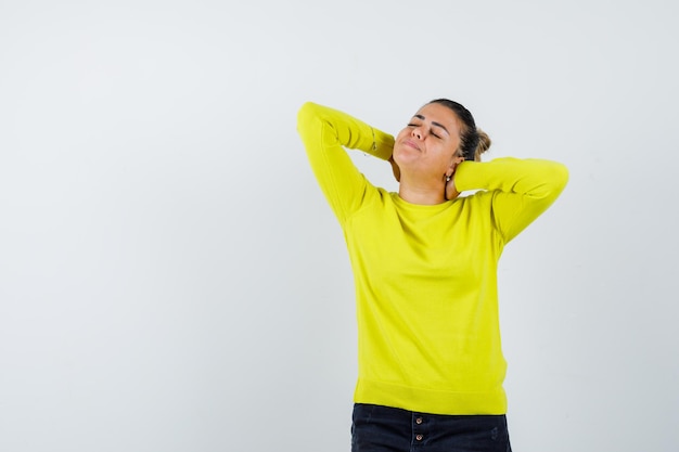 Jeune femme tenant les mains derrière la tête en pull jaune et pantalon noir et à l'air détendu