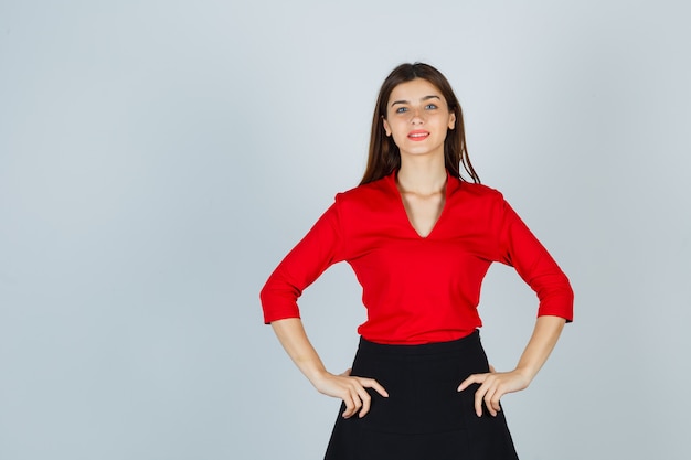 Jeune femme tenant les mains sur les hanches en chemisier rouge, jupe noire et à la joyeuse