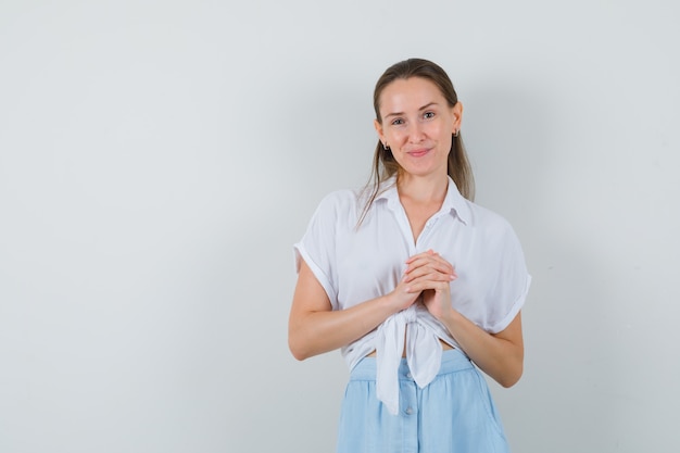 Jeune femme tenant les mains jointes en chemisier et jupe et à la confiance