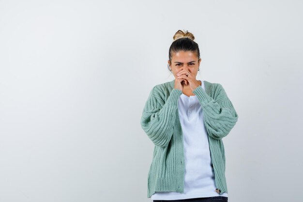 Jeune femme tenant les mains jointes près de la bouche en t-shirt, veste et l'air confiant