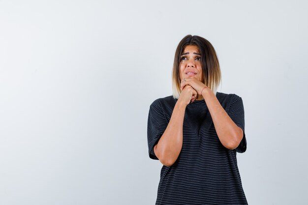 Jeune femme tenant les mains jointes en robe polo et à la recherche d'espoir. vue de face.