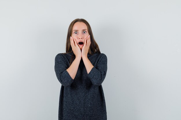 Jeune femme tenant les mains sur les joues en chemise décontractée et à la choqué