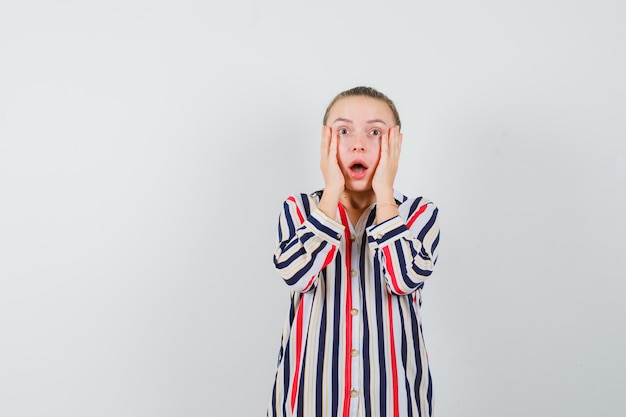 Jeune femme tenant les mains sur les joues en chemise rayée et à la choqué