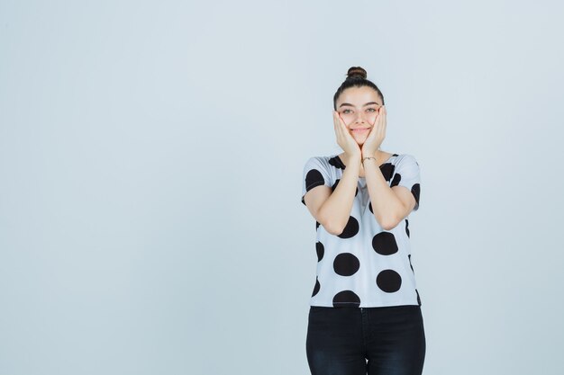 Jeune femme tenant les mains sur les joues en t-shirt, jeans et à la recherche de mignon. vue de face.