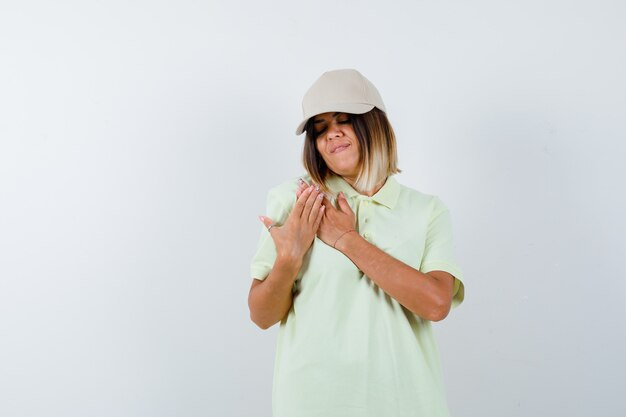 Jeune femme tenant les mains sur la poitrine en t-shirt, casquette et à la recherche d'espoir. vue de face.