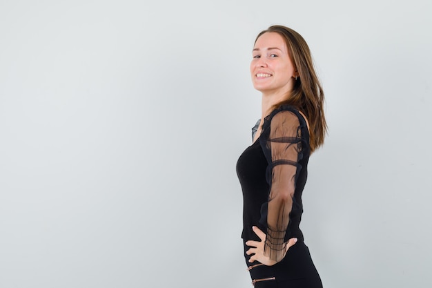 Jeune femme tenant les mains sur sa taille tout en regardant de côté en chemisier noir et à la hale. .