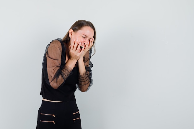 Jeune femme tenant les mains sur son visage tout en criant en chemisier noir et à la compliqué