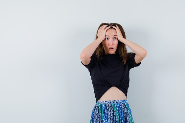 Jeune femme tenant les mains sur la tête en t-shirt noir et jupe bleue et à stressé