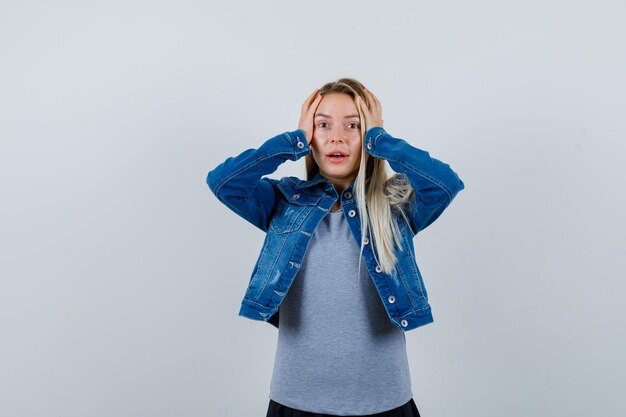 Jeune femme tenant les mains sur la tête en t-shirt, veste en jean, jupe et à l'air oublieux.