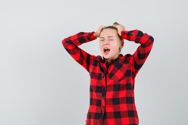 Jeune femme tenant les mains sur la tête tout en criant en chemise à carreaux et à la