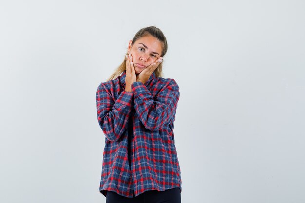 Jeune femme tenant les mains sur le visage en chemise à carreaux et à la pensif