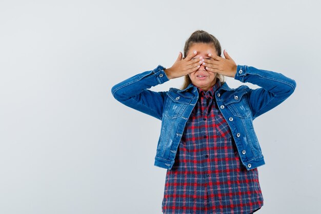 Jeune femme tenant les mains sur les yeux en chemise, veste et à la vue inquiète, de face.