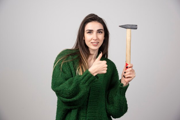 Une jeune femme tenant un marteau et montrant un pouce vers le haut.