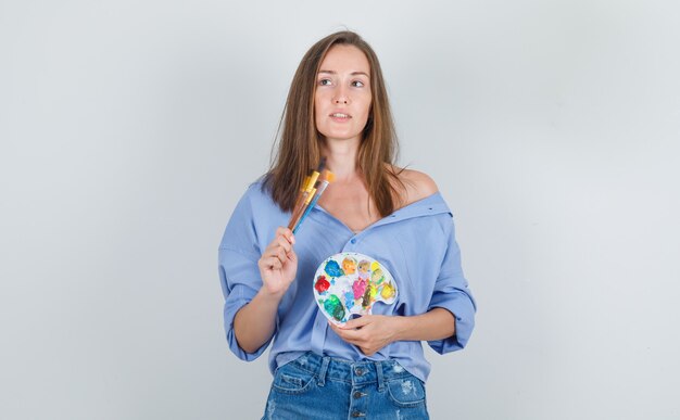 Jeune femme tenant des outils de peinture en chemise bleue, short et à la recherche d'espoir