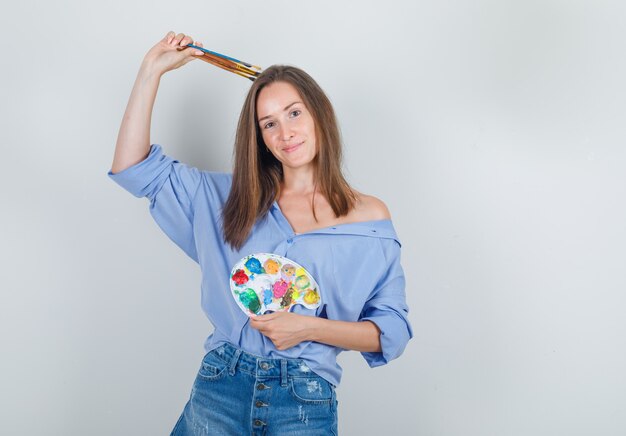 Jeune femme tenant des outils de peinture en chemise bleue, short et à la recherche d'espoir