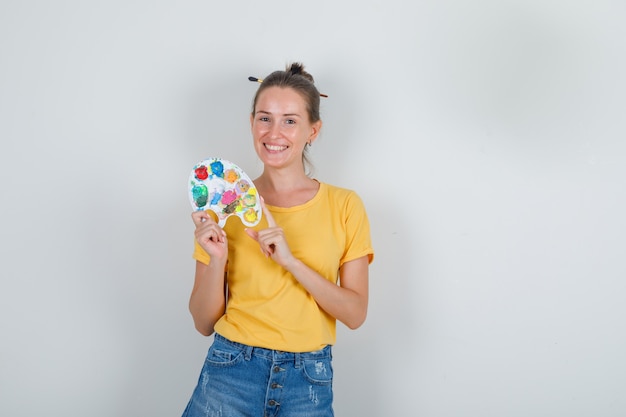 Jeune femme tenant une palette d'art en t-shirt jaune, short en jean et à la joyeuse