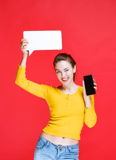 Jeune femme tenant un panneau d'information rectangle et un smartphone noir