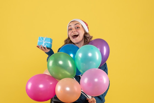 jeune femme tenant petit cadeau et ballons sur jaune