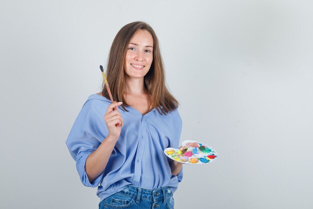 Jeune femme tenant un pinceau et une palette en chemise bleue, un short et à l'optimiste